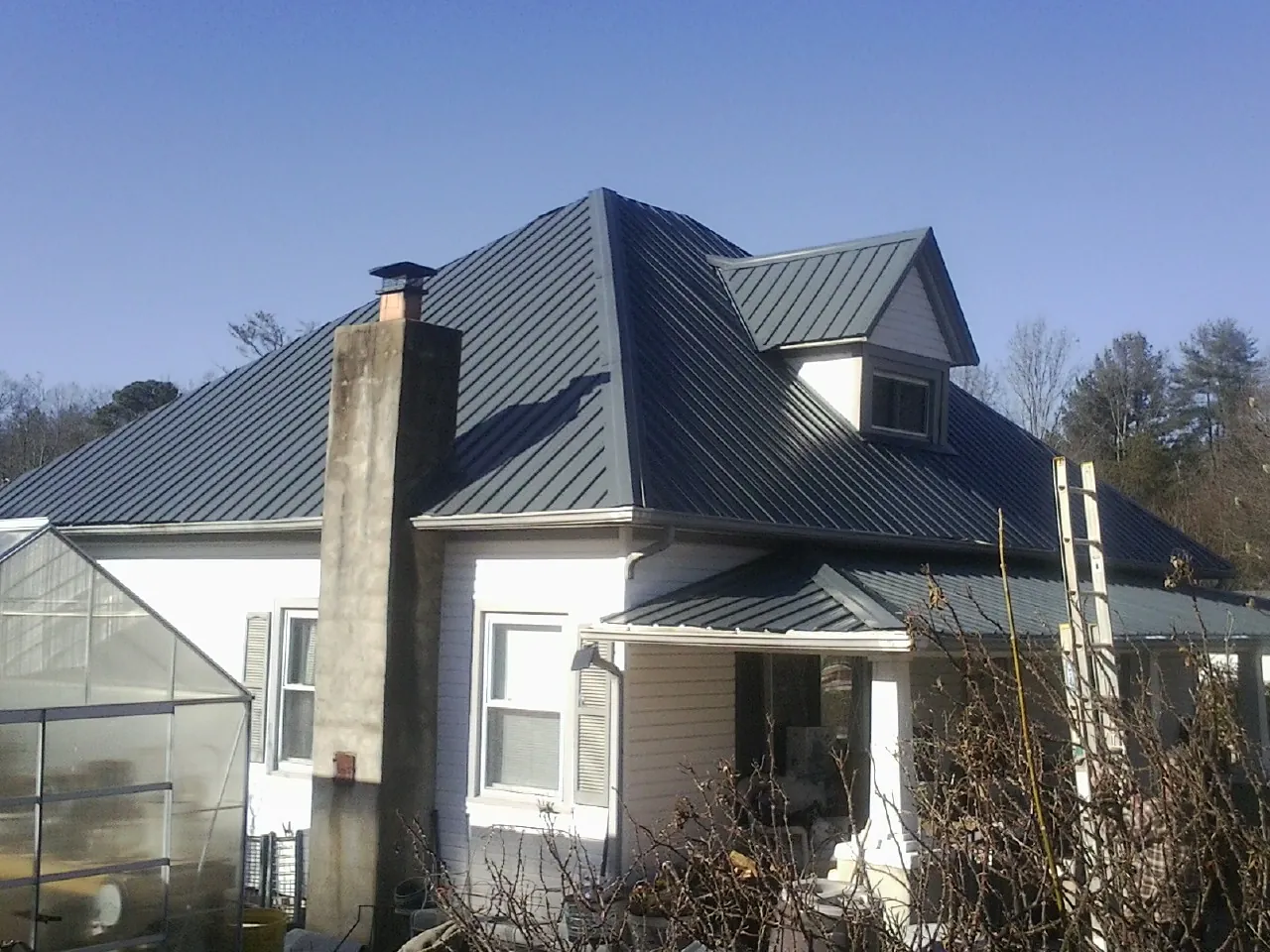 Dark blue standing seam metal roof on a white farmhouse with dormer — Slate & Tile Roof Repair by Roofing Brothers in Mooseheart