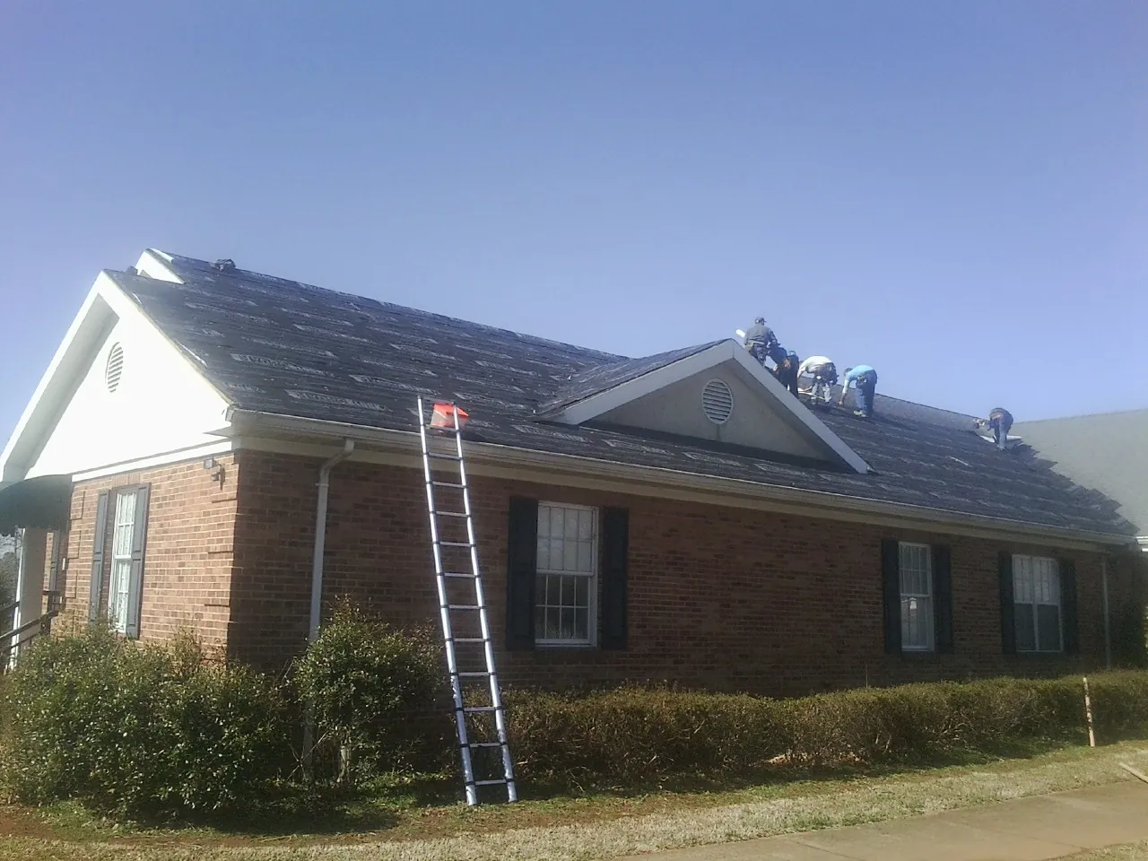 Crew tearing shingles off a brick ranch roof with a ladder set — Emergency Roof Repair work by our crew in Mooseheart