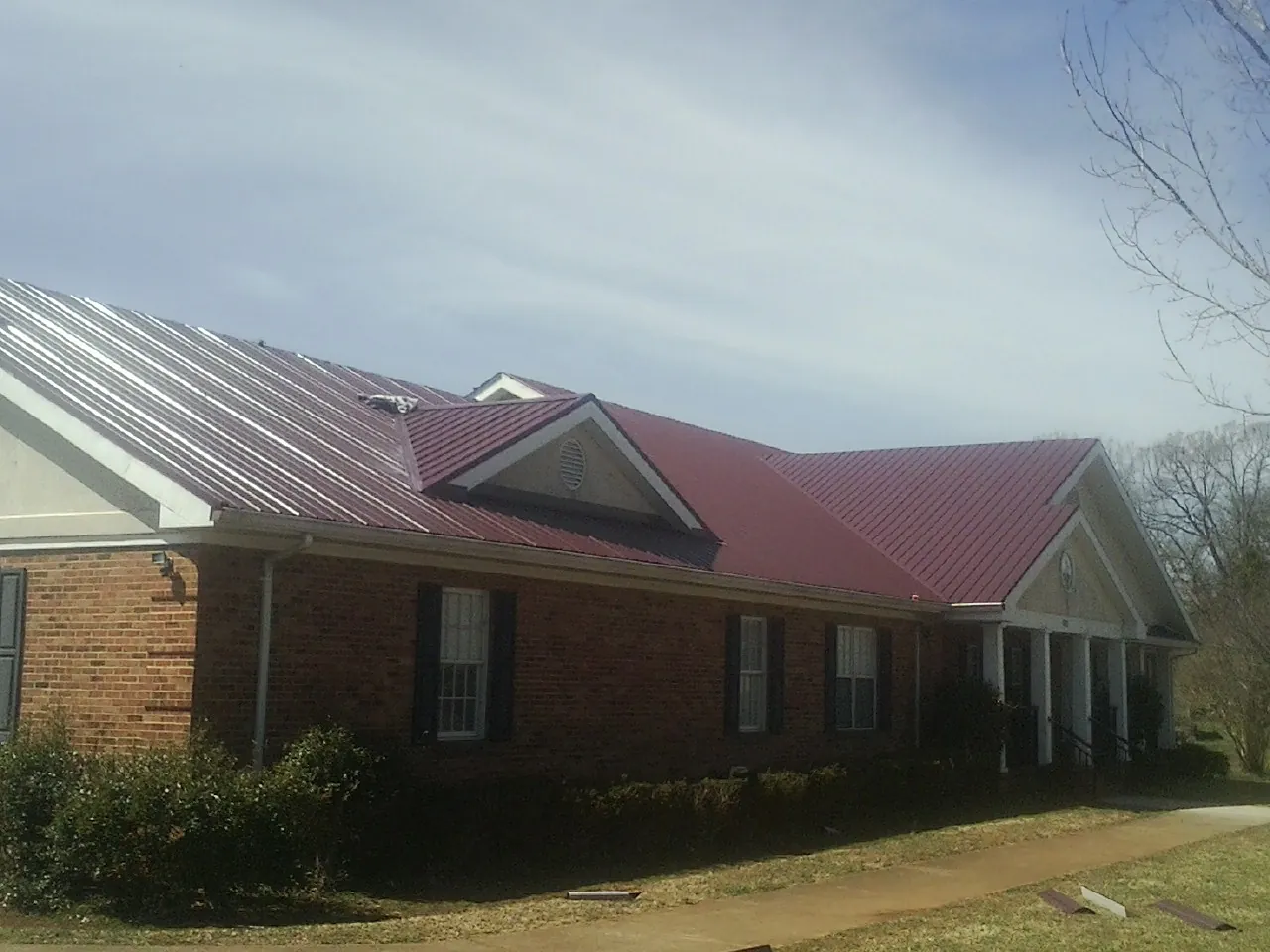 Red metal roof with gabled entries on a long brick building, from a Hail Damage Roof Repair job in Mooseheart
