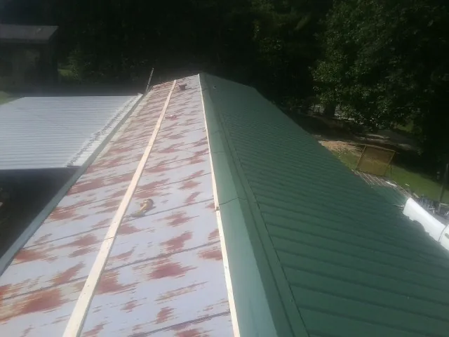 Old rusted panels beside newly installed green metal roofing — Wind Damage Roof Repair by Roofing Brothers in Mooseheart