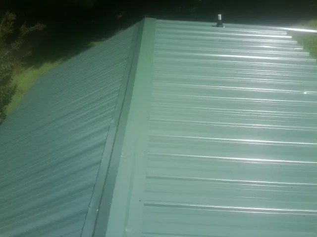 New green metal panels meeting at the ridge of a roof — Flat Roof Repair work by our crew in Mooseheart
