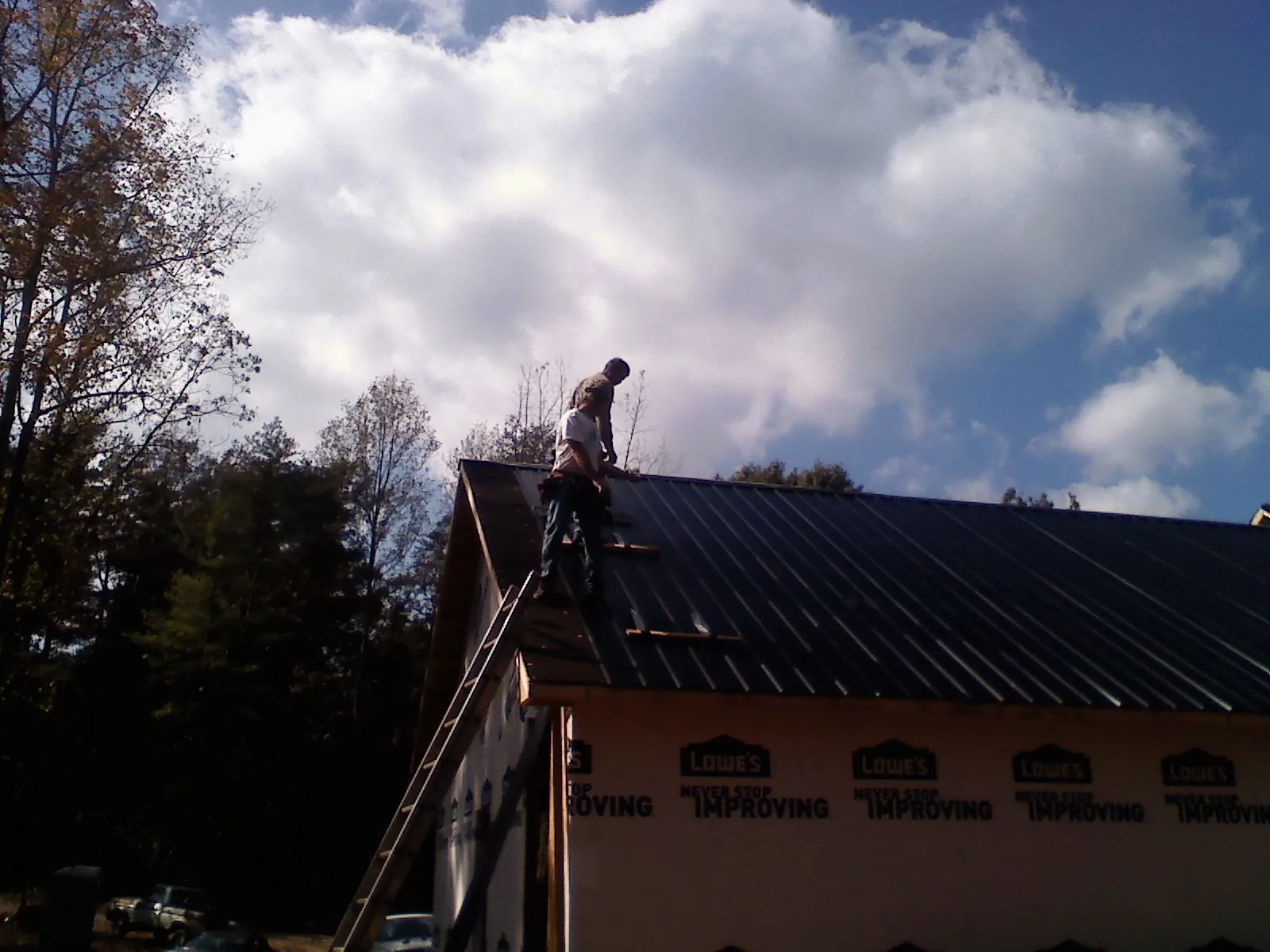 Roofer fastening dark metal panels high against a cloudy sky, from a Roof Inspection job in Mooseheart