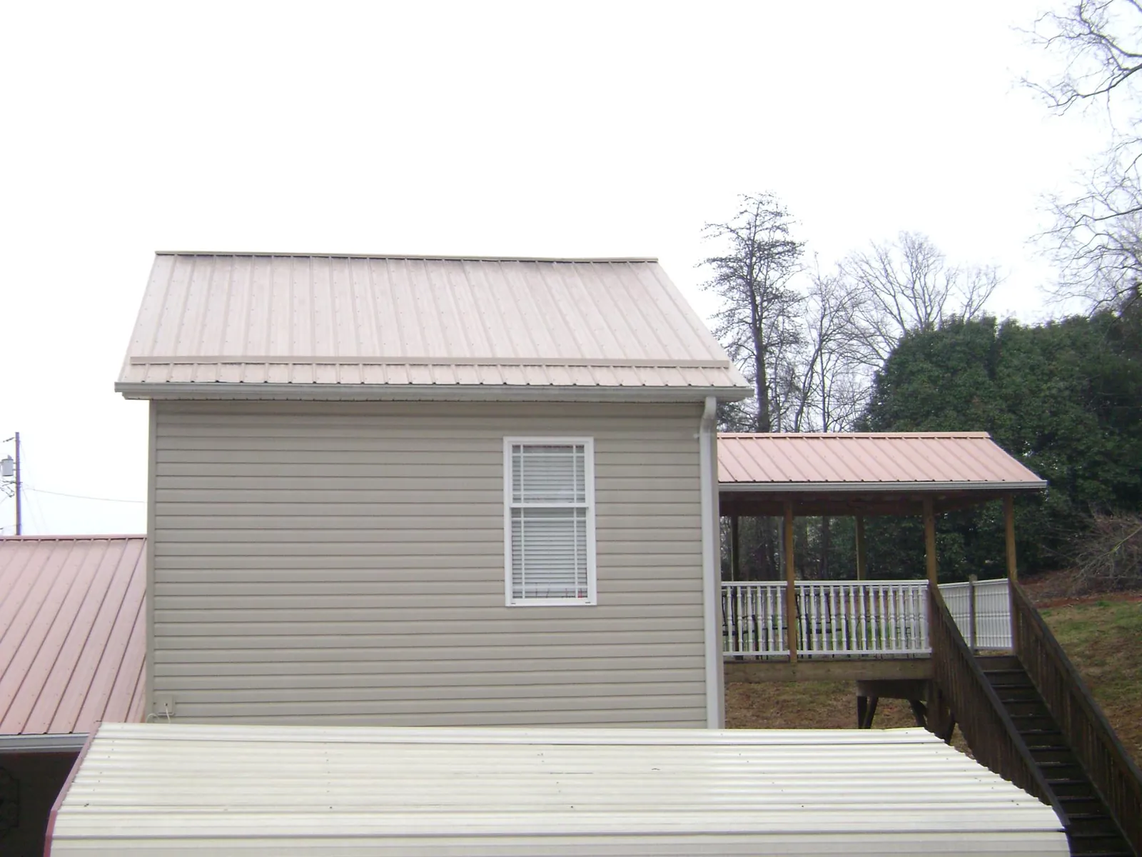Tan metal roofs on a two story addition and attached porch, from a Roof Replacement job in Mooseheart